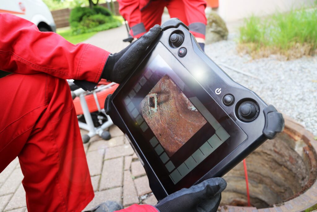Sewer camera inspection with plumber holding receiver showing live feed of video inside sewer line